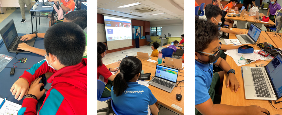 Children in a classroom workshop using laptops, with a teacher presenting on a projector screen at the front.